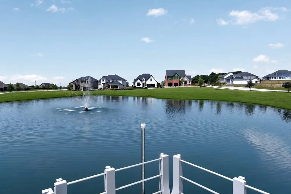 Community pond with fountain, surrounding homes, and paths at The Ranch at Uptown Celina